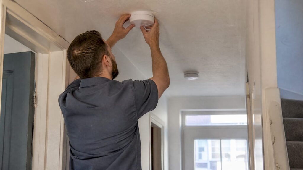 Electrician installing wireless smoke alarm in hallway