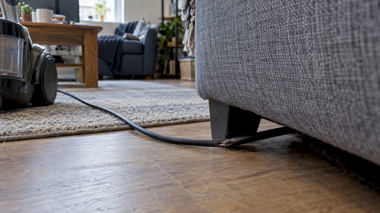Worn appliance cable pinched beneath a sofa